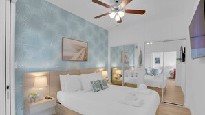 A modern bedroom with a large bed, bedside tables, a ceiling fan, and a mirror.