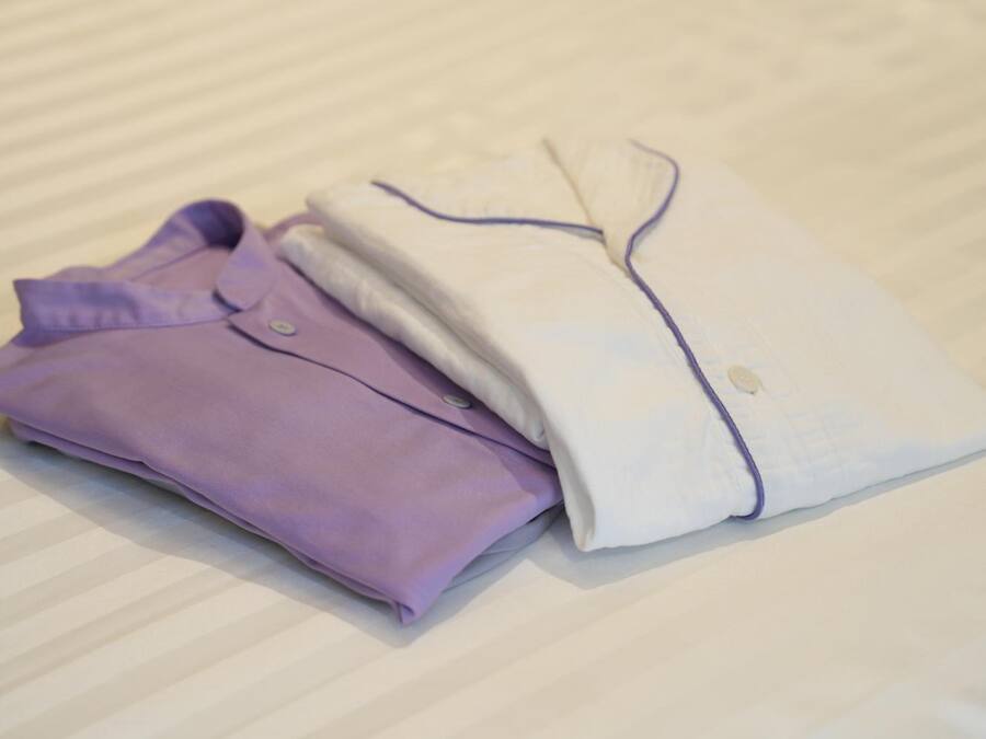 Two neatly folded shirts, one purple and one white, on a bed with a striped bedspread.