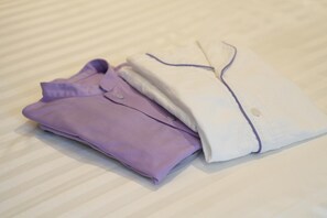Two neatly folded shirts, one purple and one white, on a bed with a striped bedspread. - Hotel Ole Inn (Shizuoka)
