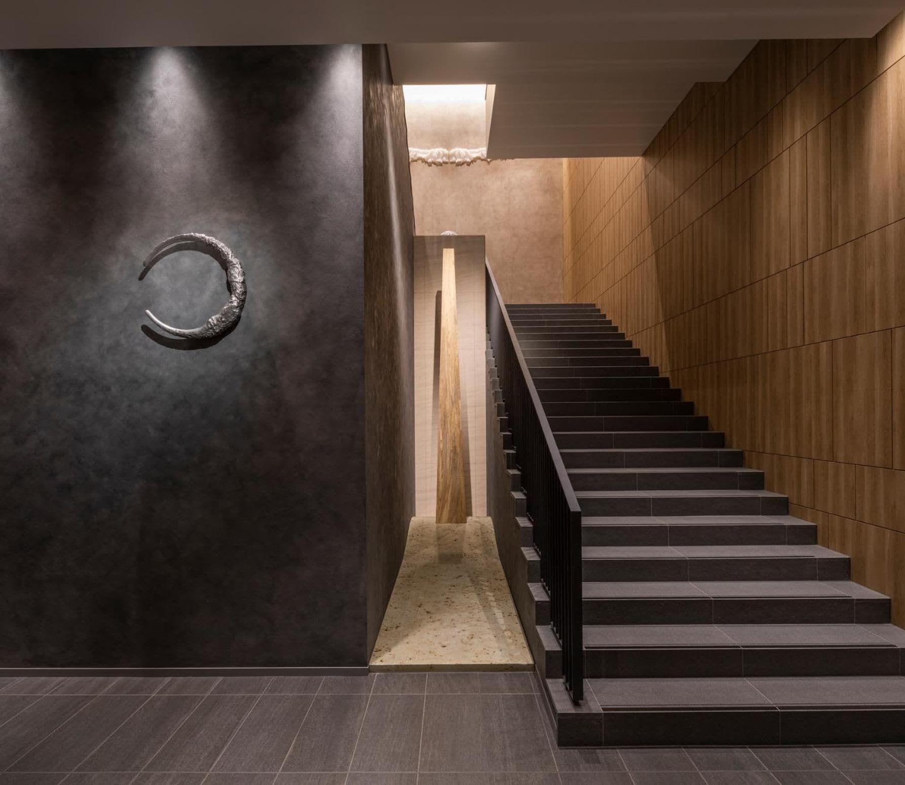 Un interior moderno con una escalera, paredes oscuras y un suelo con textura.