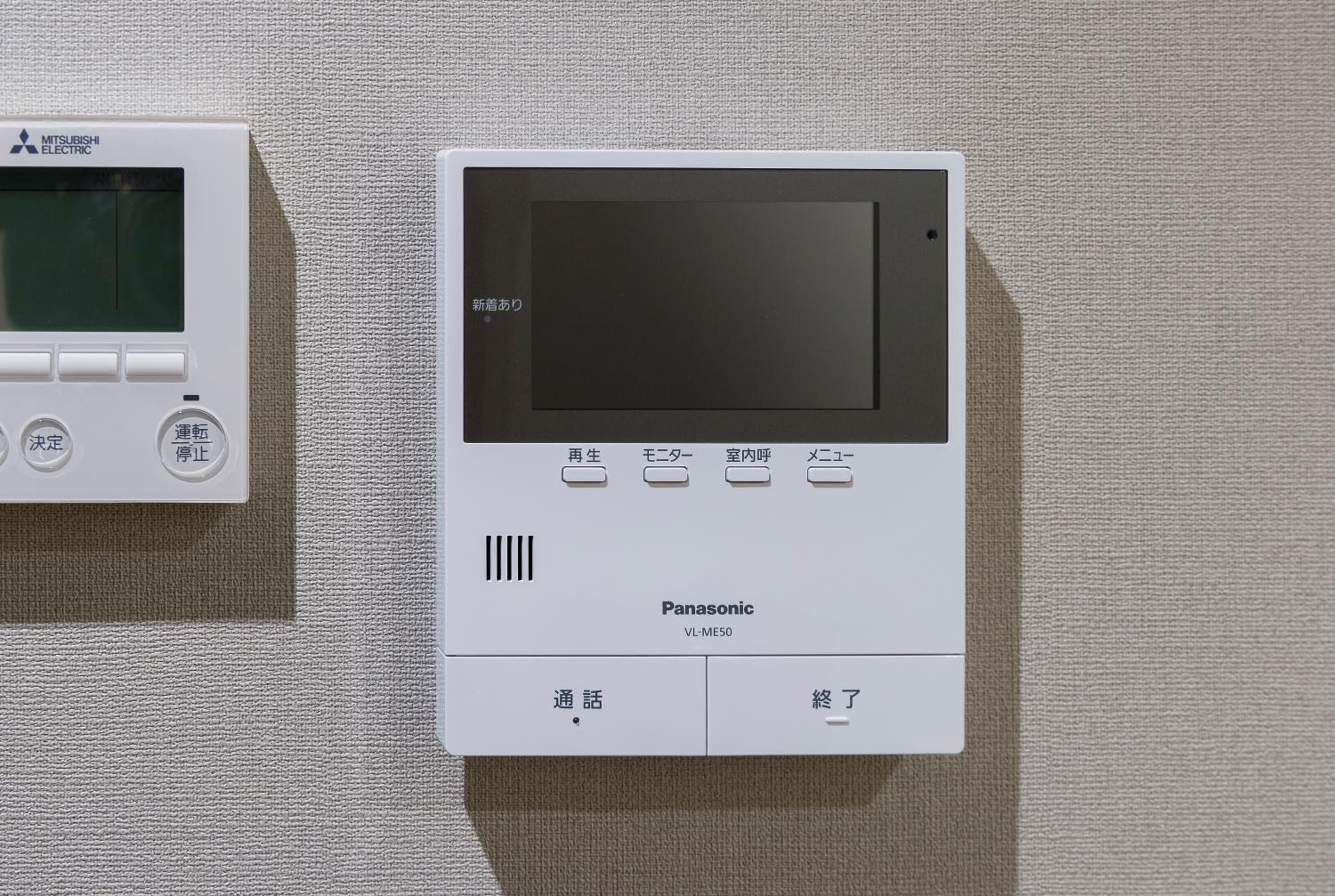 Two electronic devices, one labeled 'Mitsubishi Electric' and the other 'Panasonic,' mounted on a textured wall.