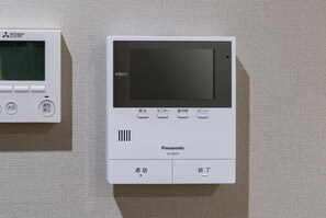 Two electronic devices, one labeled 'Mitsubishi Electric' and the other 'Panasonic,' mounted on a textured wall. - Hotel Ole Inn (Shizuoka)