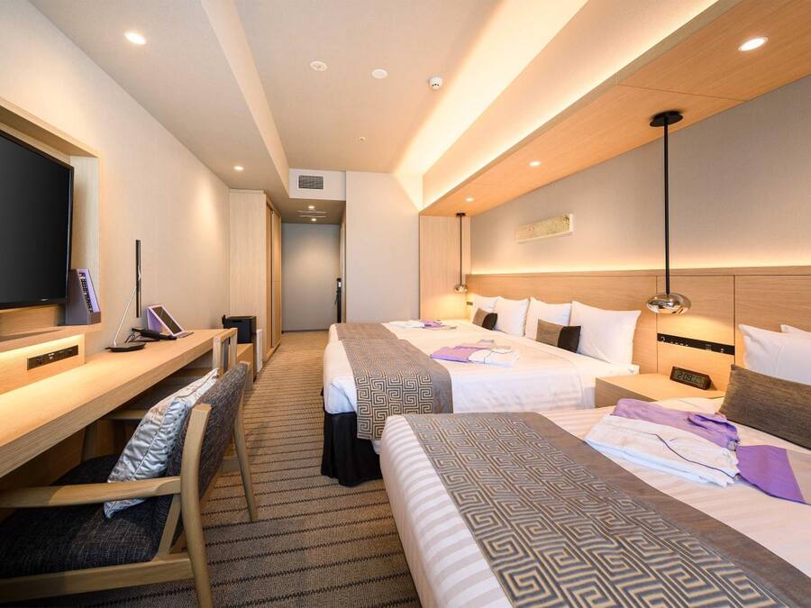 A hotel room with two beds, a desk, a chair, and a television.