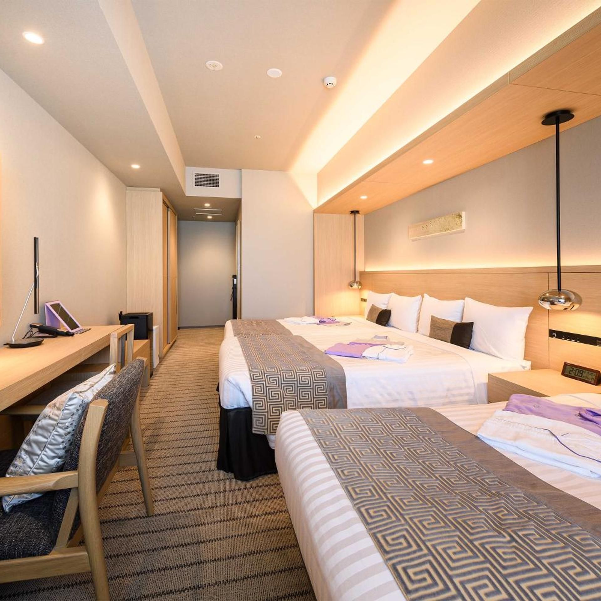 A hotel room with two beds, a desk, and a chair.