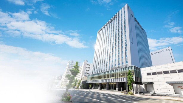 A modern hotel building with a prominent entrance and a clear sky. - Hotel Ole Inn (Shizuoka)