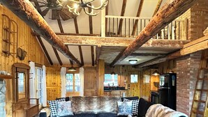 A rustic cabin interior with a large wooden dining table, a sofa set, and a chandelier. - Rustic Log Cabin near National Park with Hot Tub & Mountain Views (Allenspark)