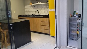 Eine moderne Küche mit weißen und gelben Schränken, einer schwarzen Arbeitsplatte und einer Glastür zum Balkon.