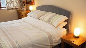 A neatly made bed with striped bedding, two bedside tables with lamps, and a floral curtain. - The Stable, Aberystwyth (Aberystwyth)