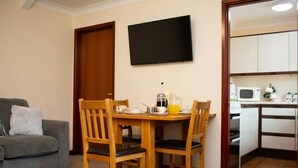 A compact living space with a dining area, kitchenette, and a TV mounted on the wall.