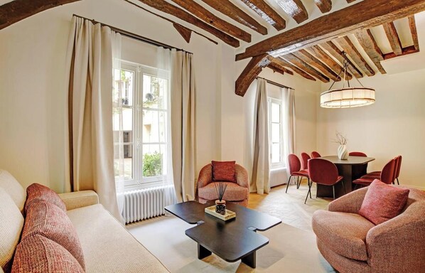 A spacious living room with a sofa, armchairs, a dining table with chairs, and a ceiling with exposed wooden beams.