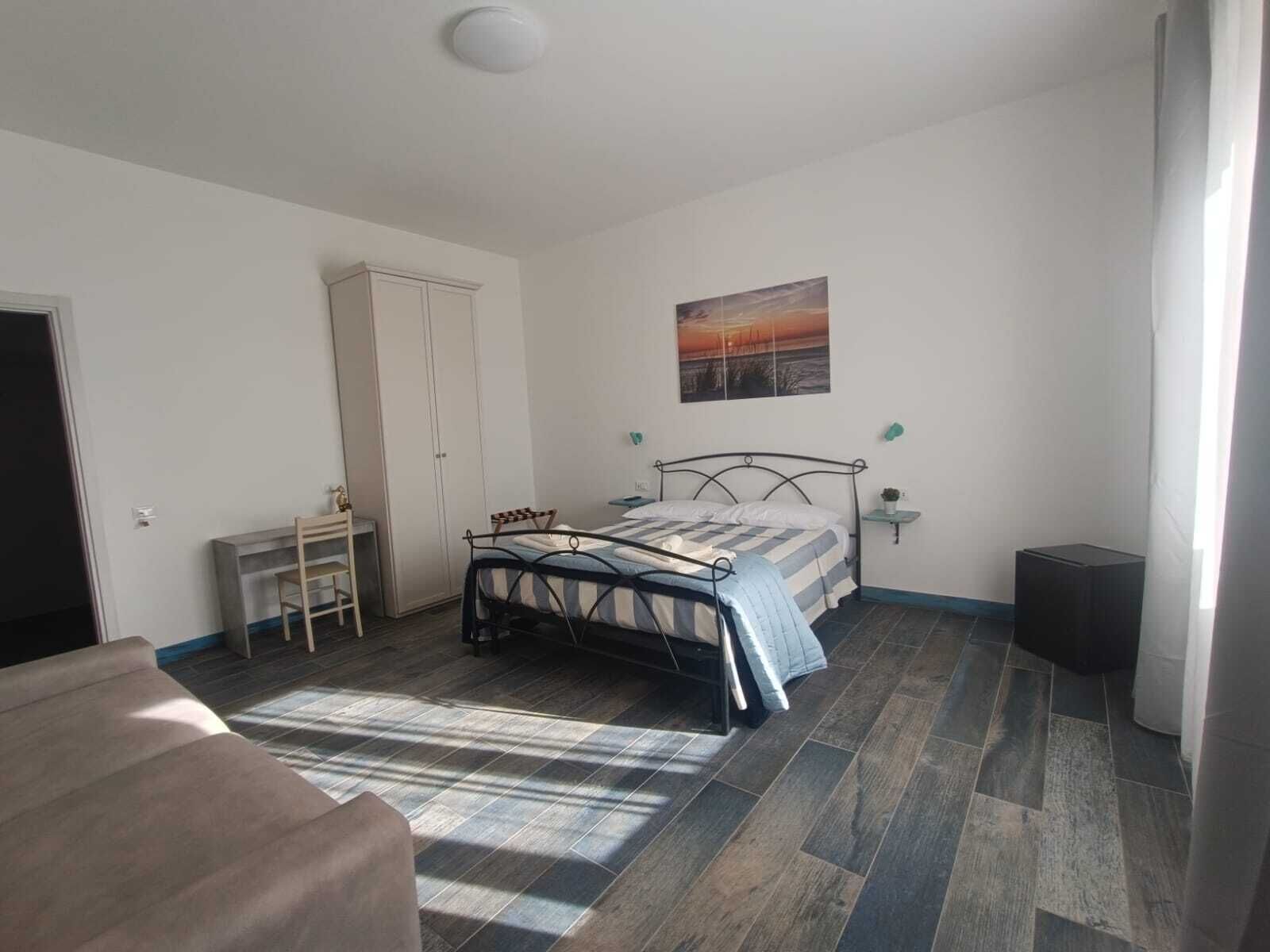 A bedroom with a bed, a desk, a wardrobe, and a painting on the wall.