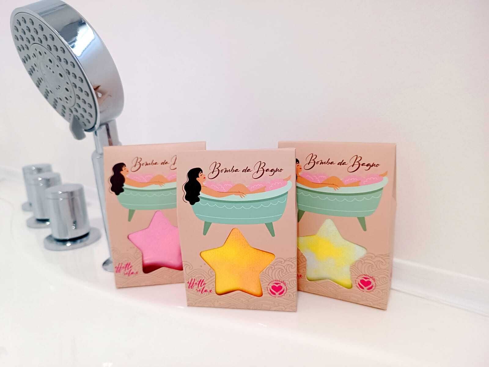 Tres bombas de baño con forma de estrella y una ilustración de escena de baño en el empaque, colocadas junto a un cabezal de ducha.