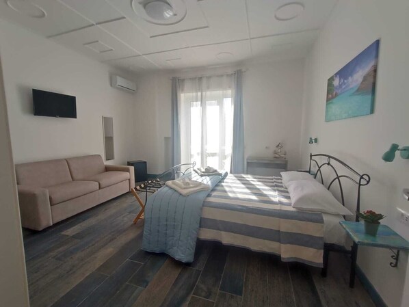 Un dormitorio con cama, sofá, escritorio y ventana con cortinas.