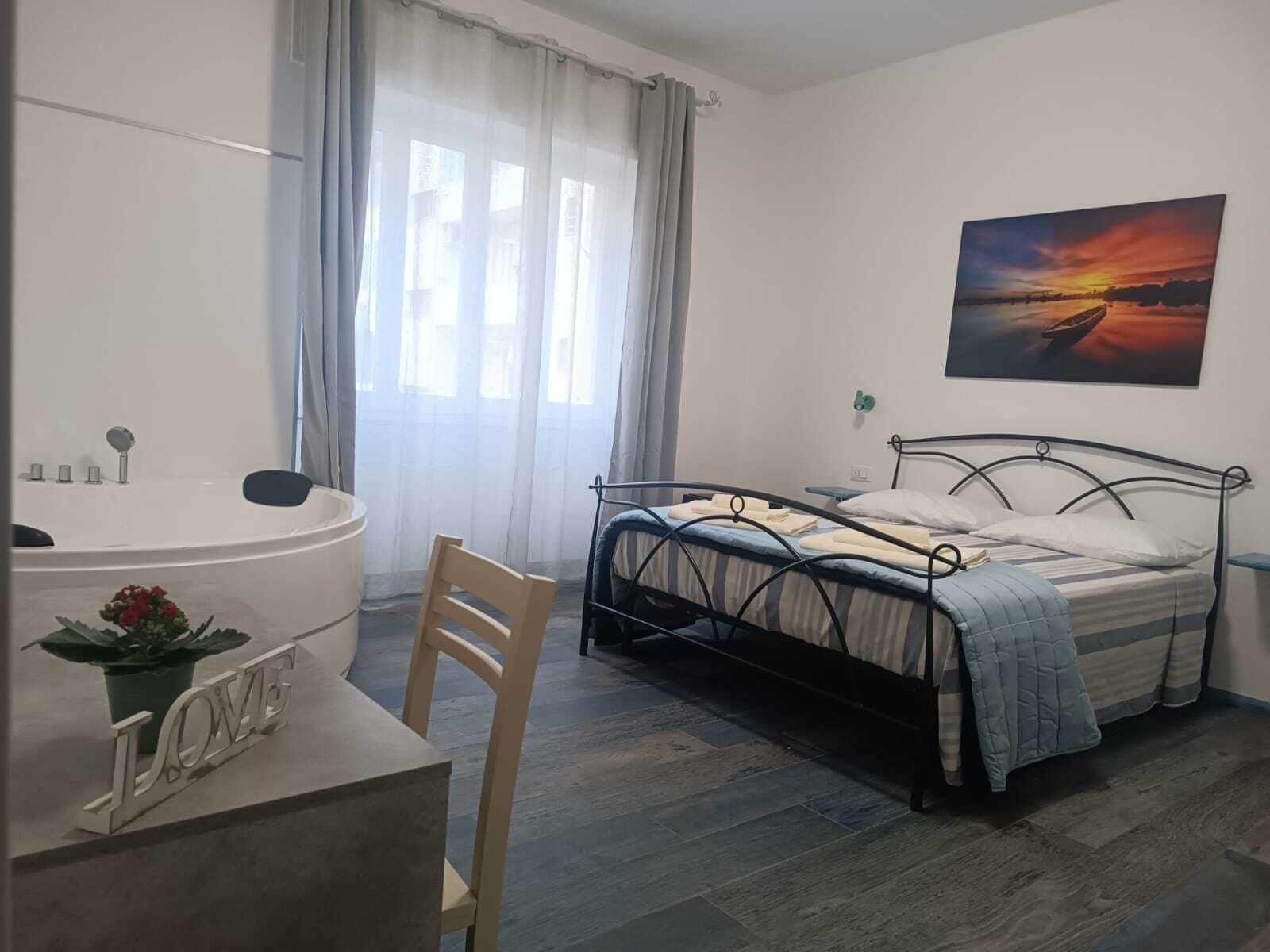 Un dormitorio con cama, escritorio, silla, bañera y un cuadro en la pared.