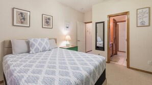 Quarto com cama, mesa de cabeceira, abajur e quadros na parede.
