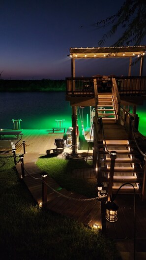 Een houten terras met een overdekte zithoek, een steiger en uitzicht op het water.