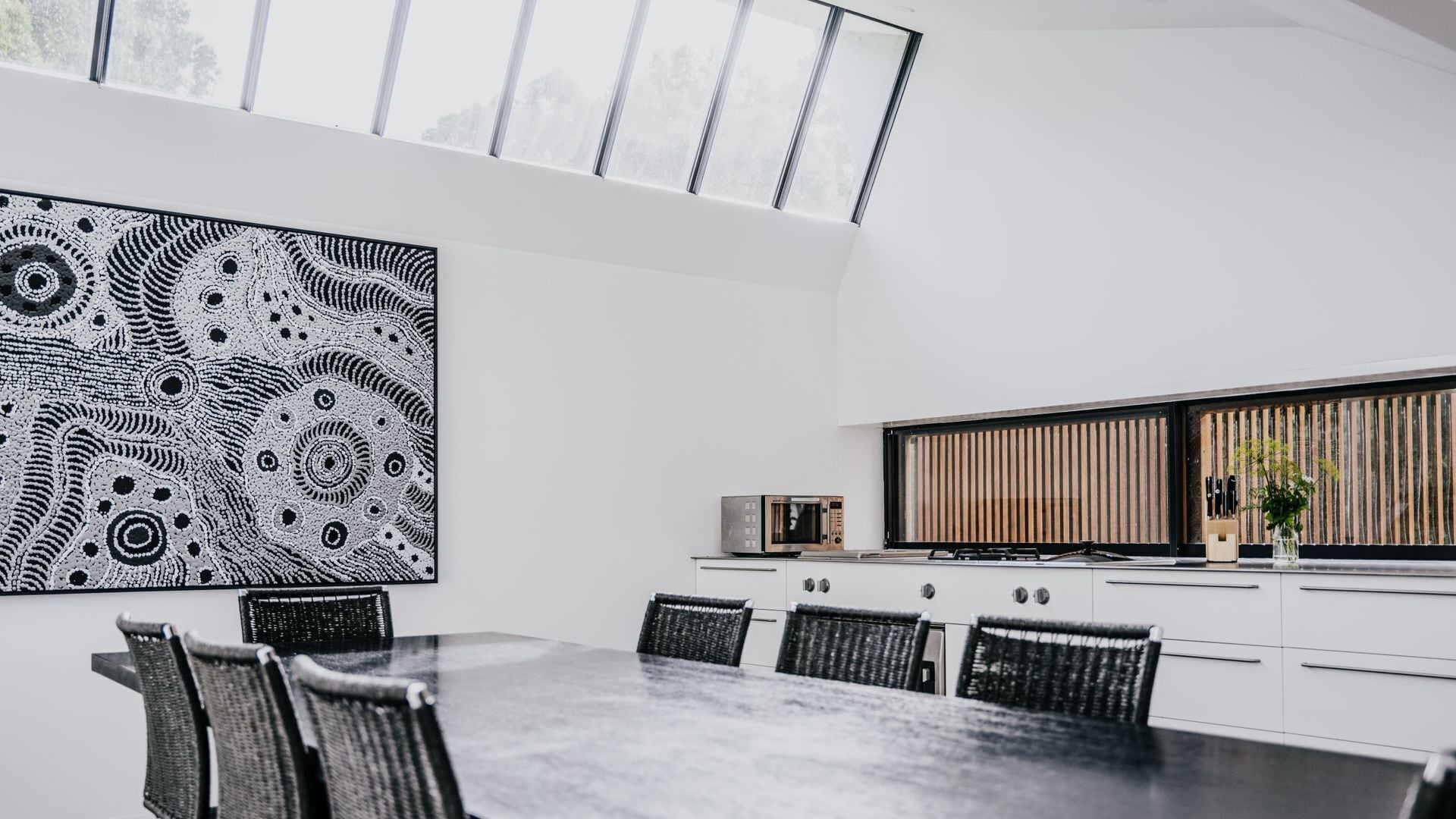 Una cocina moderna con armarios blancos, una mesa de comedor con sillas y un cuadro abstracto grande en la pared.