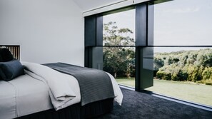 A modern bedroom with a large window, a bed with a black headboard, and a view of a green landscape. - Alkina Lodge Milu Great Ocean Road (Wattle Hill)