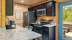 A compact kitchen with dark cabinetry, a stainless steel refrigerator, a microwave, and a granite countertop. - Close to Dollywood-Hot Tub & Kids Closet (Pigeon Forge)