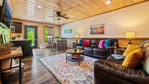 A cozy living room with a leather couch, a coffee table, and a rug. There is a dining area with a table and chairs. - Close to Dollywood-Hot Tub & Kids Closet (Pigeon Forge)
