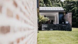 A modern house with a brick exterior, a small patio with a chair, and a lawn. - Alkina Lodge Nuru (Wattle Hill)
