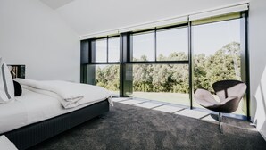 A bedroom with a large window, a bed, a chair, and a view of trees. - Alkina Lodge Nuru (Wattle Hill)