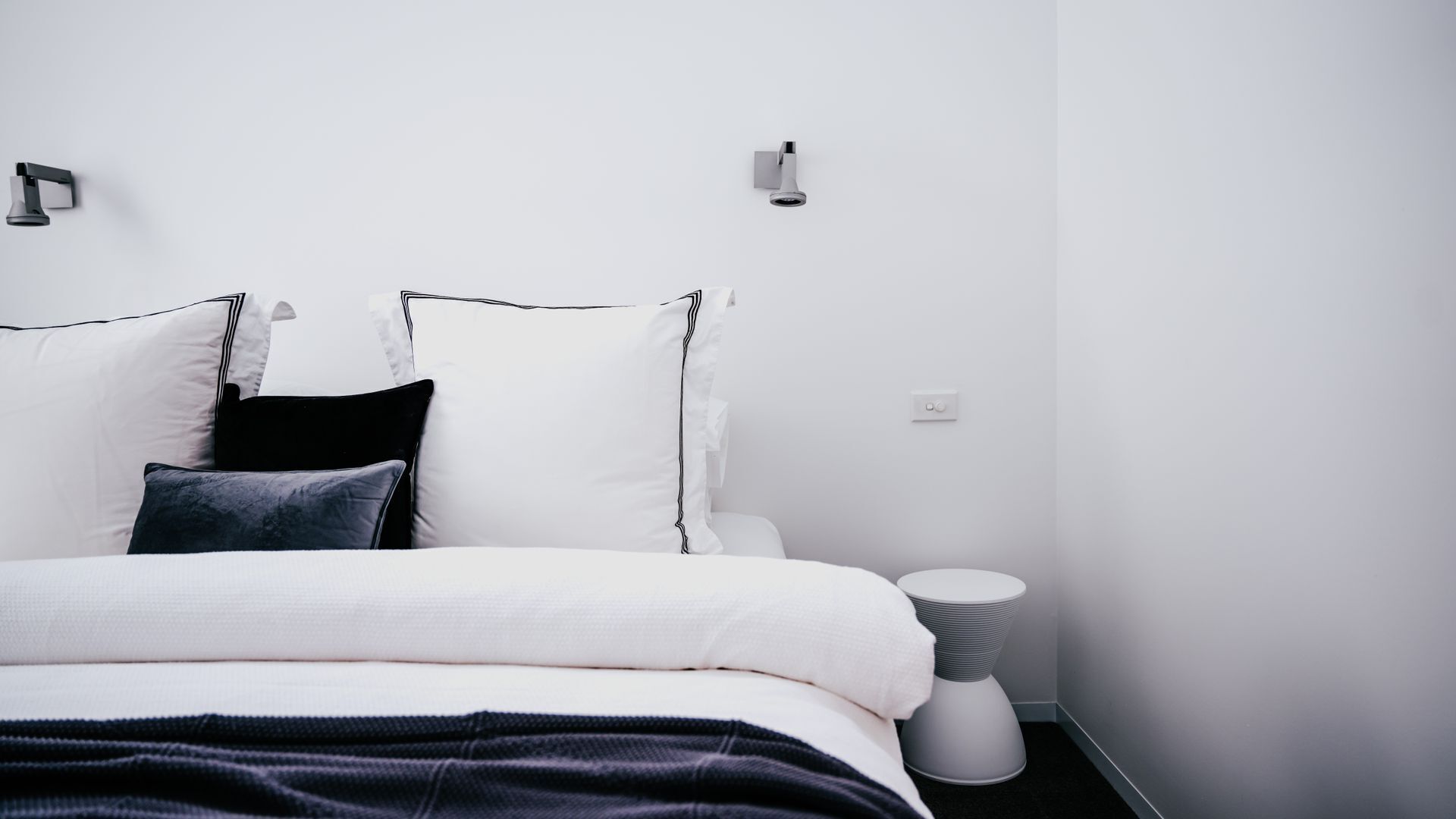 A modern bedroom with a neatly made bed, a bedside table, and a wall-mounted light fixture.