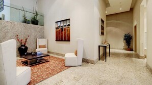 Un hall d’entrée spacieux avec un plafond haut, un sol en marbre et un coin salon moderne avec des chaises blanches et une table basse.