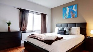 Une chambre à coucher moderne avec un grand lit, une tête de lit sombre et un tableau accroché au mur.