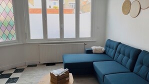 A living room with a blue sofa, a wooden coffee table, and a view of a street through large windows.