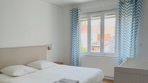 A bedroom with a bed, a nightstand, a window with curtains, and a radiator.