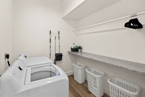 Ett tvättrum med en tvättmaskin, två tvättkorgar, en hylla med rengöringsmedel och en torkställning.