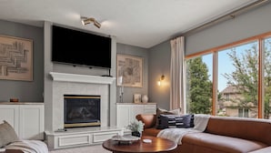 Una sala moderna con chimenea, un televisor grande montado encima y un sofá de cuero marrón, además de un tapete estampado.