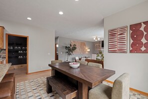 A modern dining area with a wooden table, cushioned chairs, and a decorative bowl. - Radiant Oaks Retreat - Pool - Hot tub - Game Room - Family Home (Omaha)