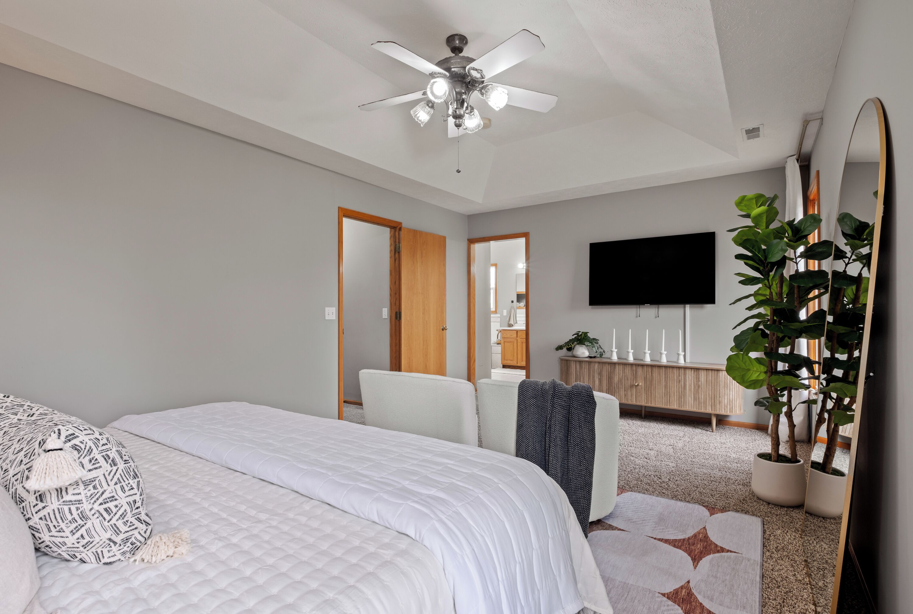 A bedroom with a bed, a ceiling fan, a TV, a mirror, and a potted plant.