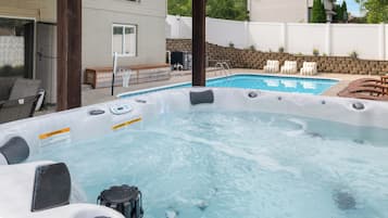 A backyard with a hot tub, a pool, and outdoor seating.