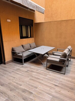 Un patio esterno con un divano, due poltrone e un tavolo.