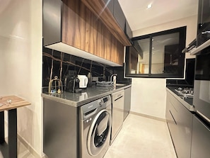 A compact kitchen with a washing machine, a coffee maker, and a microwave.