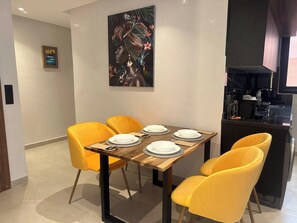 Zona pranzo con tavolo in legno, quattro sedie gialle e un quadro appeso al muro.