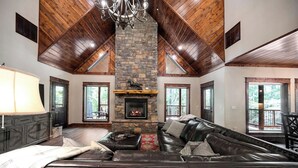 A spacious living room with a stone fireplace, leather sofa, and a chandelier. - Everpine couple's cabin retreat. Sleeps 2, pool table, hot tub, near ATV trails (Broken Bow)