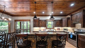 A spacious kitchen with wooden cabinets, a central island with bar stools, and a large window providing a view of the outdoors. - Everpine couple's cabin retreat. Sleeps 2, pool table, hot tub, near ATV trails (Broken Bow)