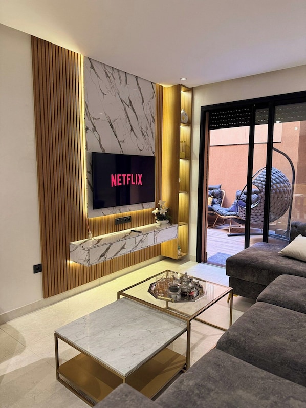 A modern living room with a flat-screen TV, a marble fireplace, and a glass coffee table.