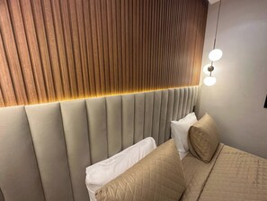 Un dormitorio moderno con cabecera acolchada, cama con ropa de cama color beige y una lámpara de pared.