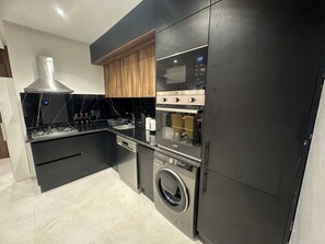 Una cocina moderna con horno empotrado, microondas y lavadora, con muebles elegantes y una campana extractora de acero inoxidable.