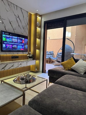 A modern living room with a flat-screen TV, a marble wall, a sofa, a coffee table, and a view of the outside.