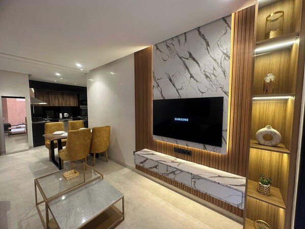 Una sala moderna con un televisor de pantalla plana, una pared de acento de mármol y un comedor con sillas y una mesa.