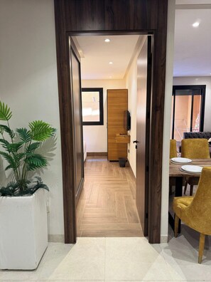 A hallway with a wooden door leading to a dining area with yellow chairs and a table.