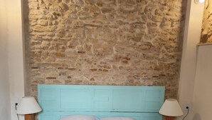 Un dormitorio con pared de piedra, cabecero turquesa y dos lámparas de noche.