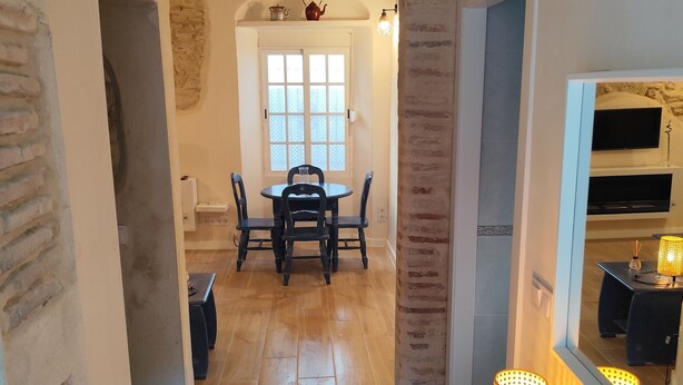 Un pasillo con piso de madera, un tapete, una mesa con velas y un comedor con una mesa y sillas.