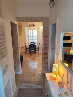 Un pasillo con piso de madera, un tapete, una mesa con velas y un comedor con una mesa y sillas.